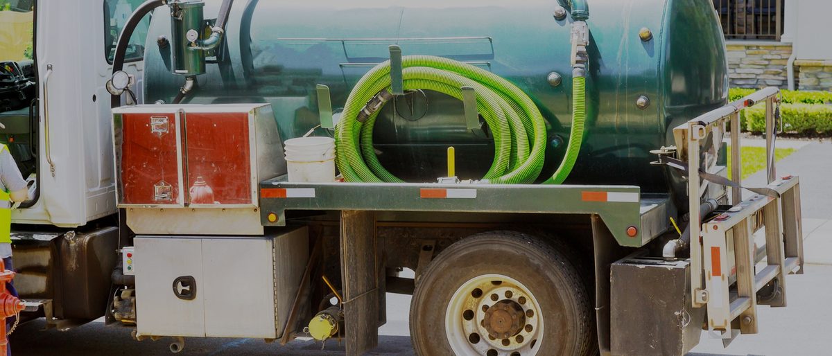 A vacuum service truck parked in a residential driveway, hose coiled on the tank